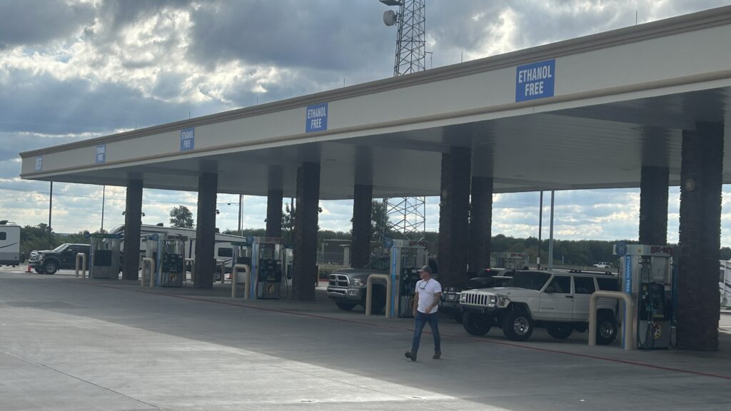 Vista frontal de um posto de combustíveis moderno com cobertura ampla, área de abastecimento e loja de conveniência.